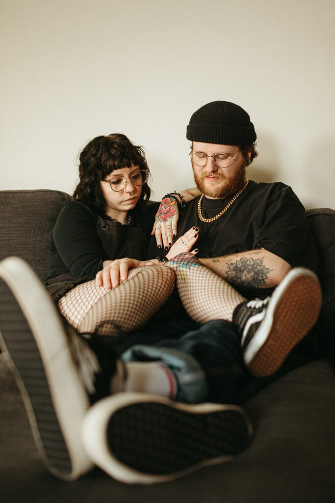 A young couple settles in together on their couch during engagement photos in their Milwaukee, WI home. 