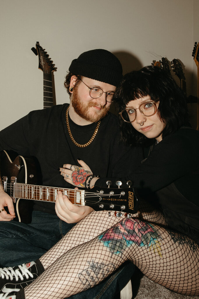 A young woman leans into her partner who is holding a guitar during engagement photos in milwaukee. 