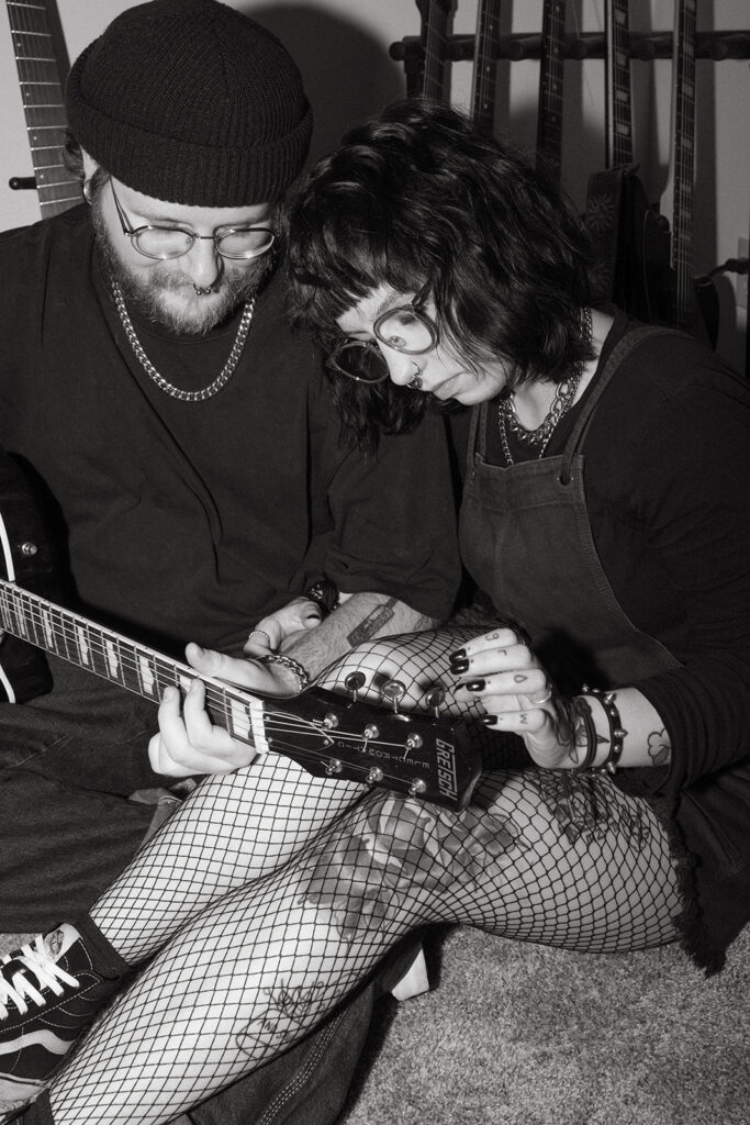 A young woman listens to her fiance play guitar during engagement photos with a Wisconsin wedding photographer. 
