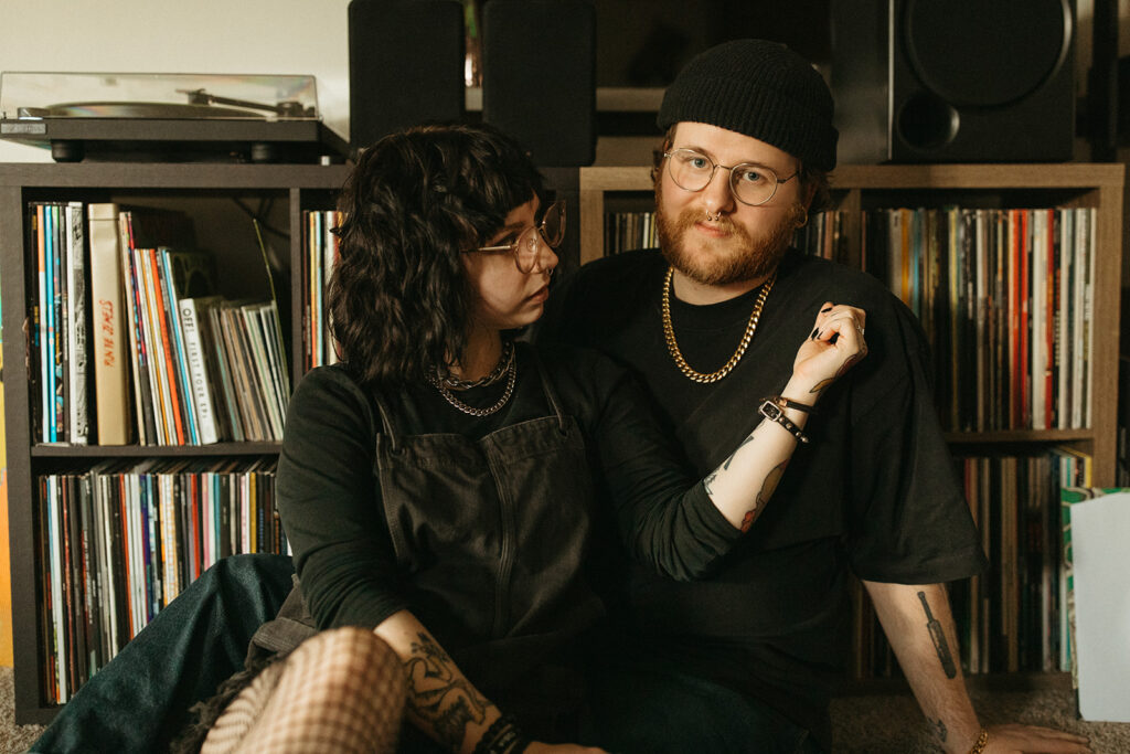 A young couple is seated on the floor of their living room before their vinyl collection during in-home engagement photos Milwaukee. 