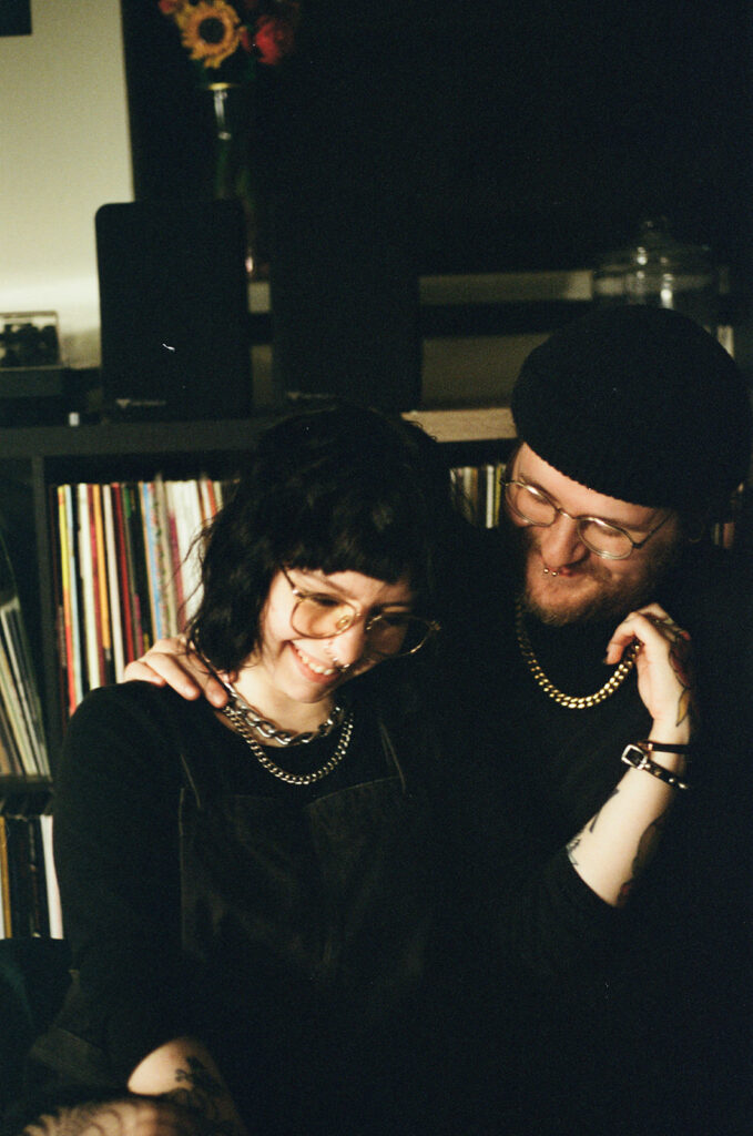A young couple laugh in their living room in a film photo taken by a Wisconsin photographer for couples. 