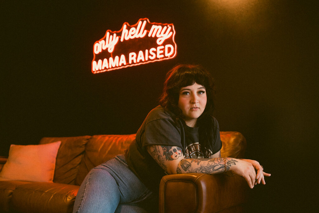 A Milwaukee hairstylist poses beneath a neon sign for a grungy brand session with a Milwaukee headshot photographer.