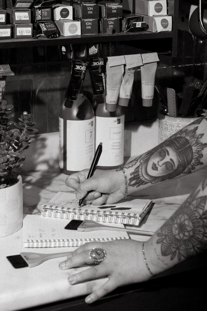 A close up black and white image shows a salon owner in Milwaukee writing color formulations during a milwaukee photography session with a brand photographer. 