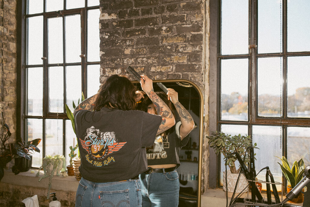 A Milwaukee salon owner combs her bangs in a mirror at Lady Luck Salon during her brand session with a Milwaukee headshot photographer. 