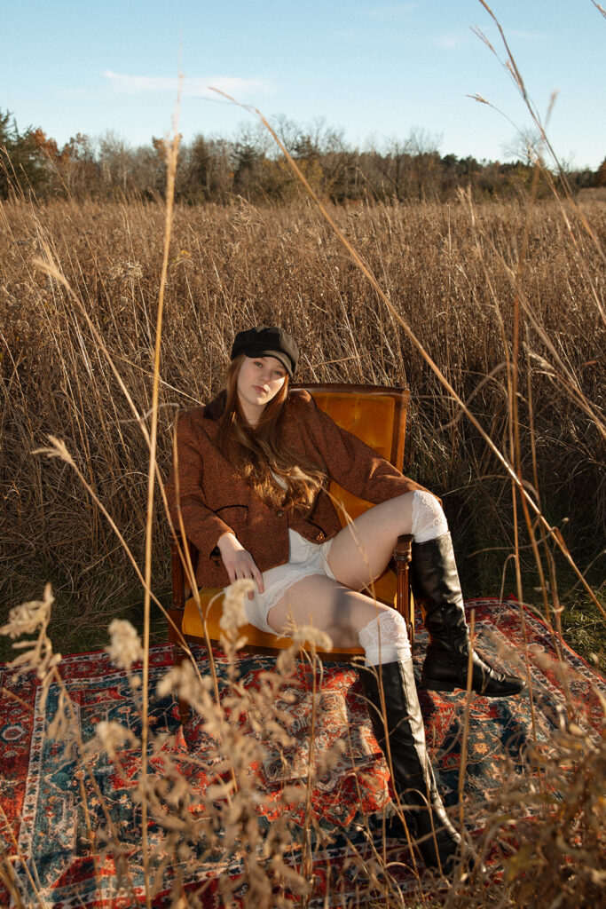 A young woman is seated on a vintage chair amongst the prairie grass at Afton State Park for her Minnesota senior pictures.
