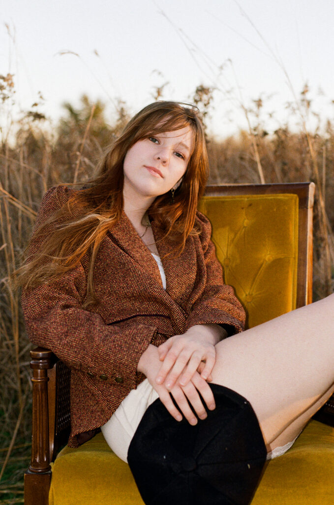 A young woman is seated on a mustard yellow vintage  chair during a photoshoot with a Minnesota senior photographer at Afton State Park 