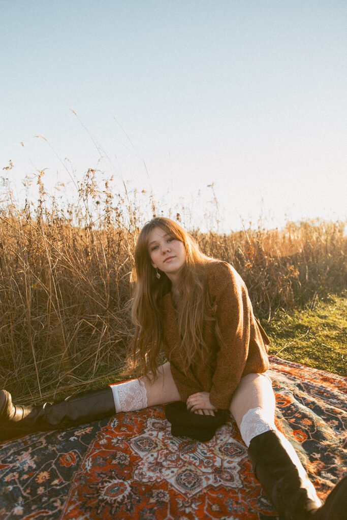 A high school senior is seated on a rug in a field at Afton State Park for her Minnesota senior photos 