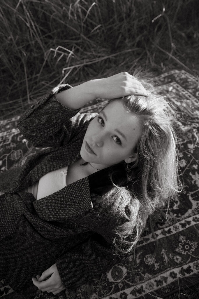 A black and white image of a high school senior posing on a vintage-inspired rug during a photoshoot with a Minnesota senior photographer. 