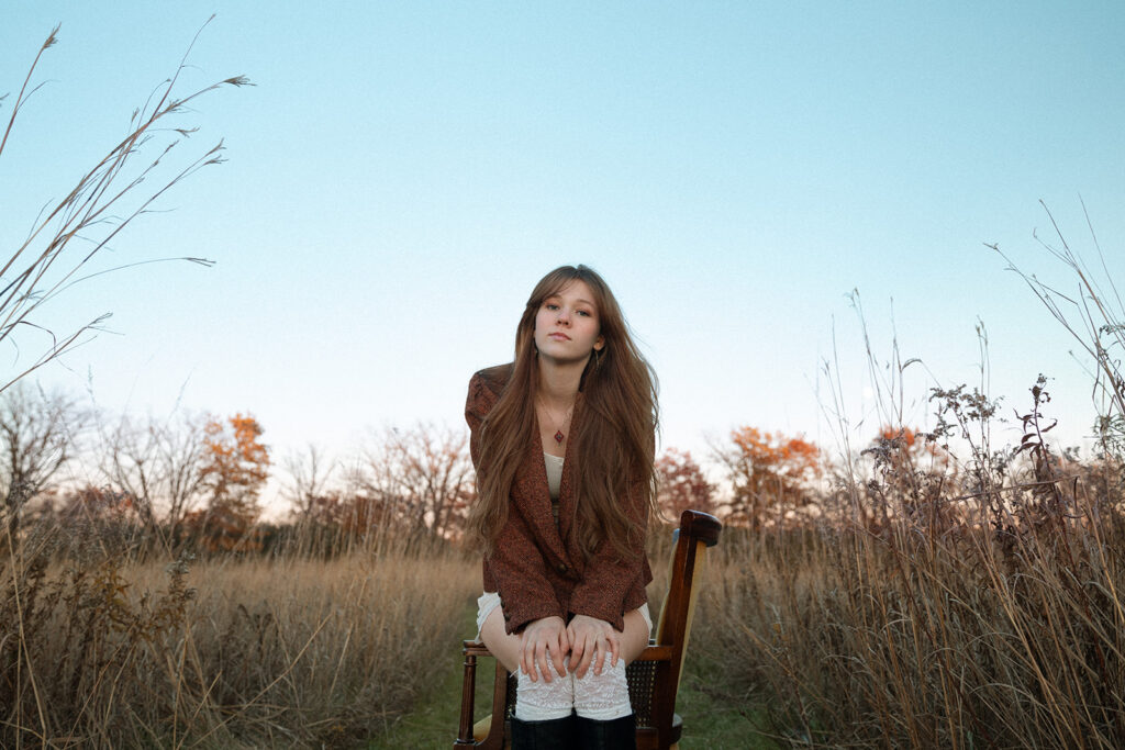 A young woman is photographed surrounded by prairie grass at golden hour for her Minnesota senior pictures. 