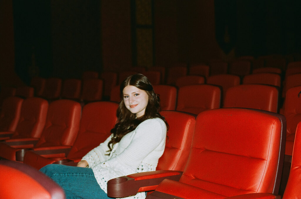 A young woman smiles from a seat in The Heights Theater during Minneapolis senior pictures.