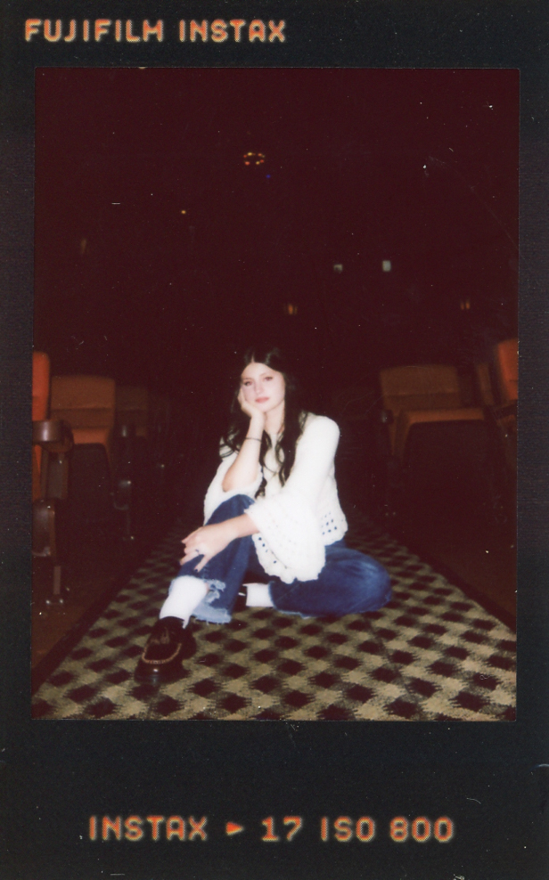 A young woman is seated on the floor of The Heights Theater during a senior photoshoot with a Minneapolis senior photographer.