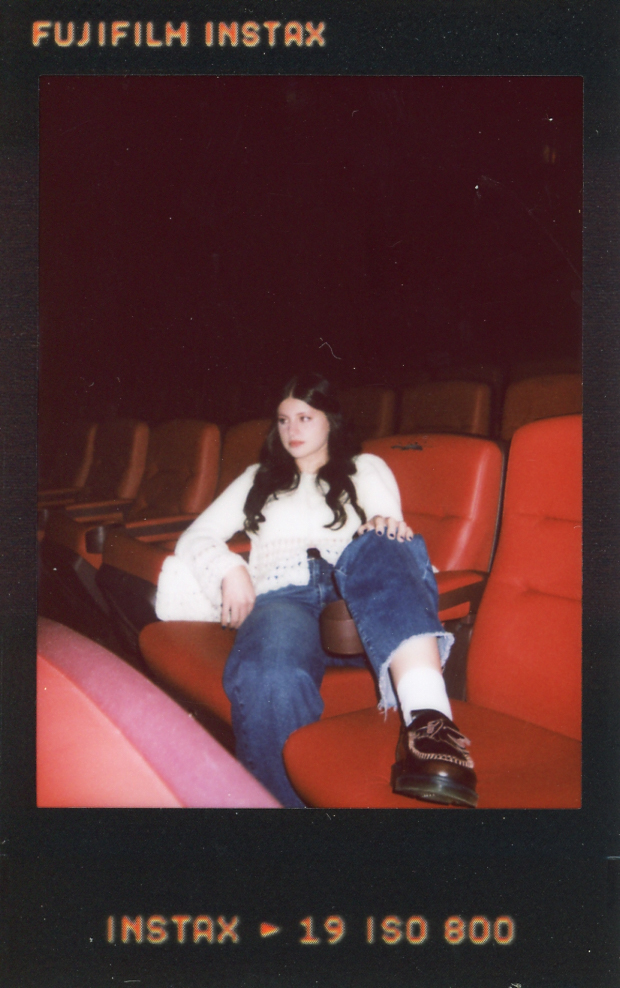 A high school senior lounges across the seats at The Heights Theater in instax film captured during Minneapolis senior pictures.
