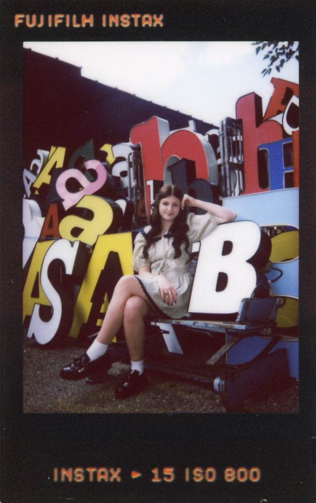 A young woman poses with signage at a local antique store in an instax film taken by a Minnesota senior photographer.