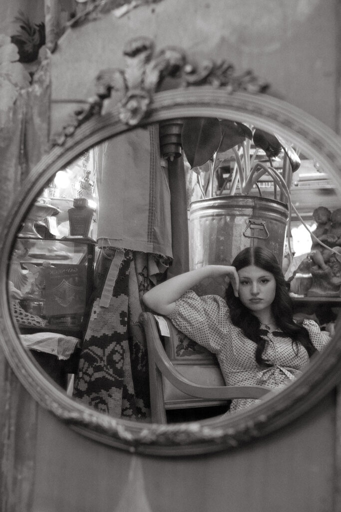 A black and white image of a young woman peering into an antique mirror during senior pictures in Minnesota.