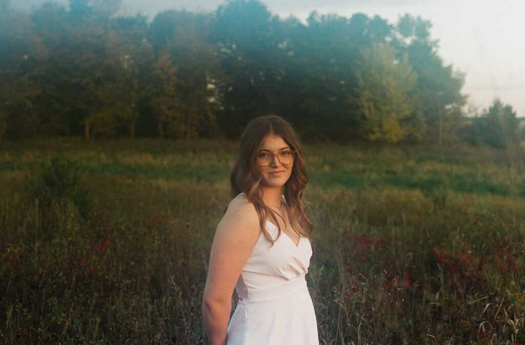 A young woman wears a white dress in a wildflower field during minneapolis senior pictures.