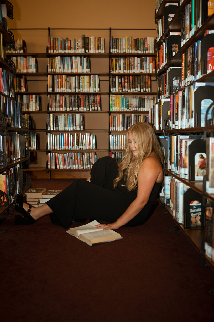 A young woman skims a hardback book in a library during senior pictures in the twin cities MN.
